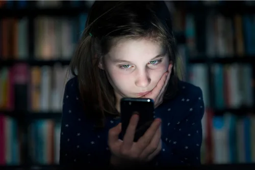 Young girl in a dark room staring at her phone